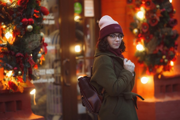 Alegre menina feliz aproveitando o tempo nevando na rua sorrindo e curtindo a vida vestindo casaco de pele elegante chapéu de malha e cachecol largo humor festivo humor de natal verdadeira felicidade