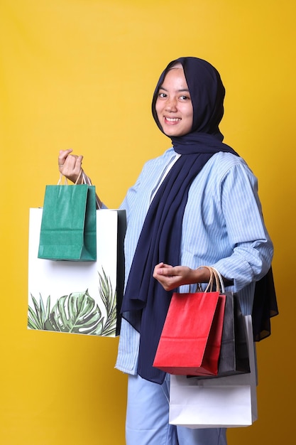 Alegre menina muçulmana animada em estilo casual usando chapéu está mostrando muitos sacos de papel de compras