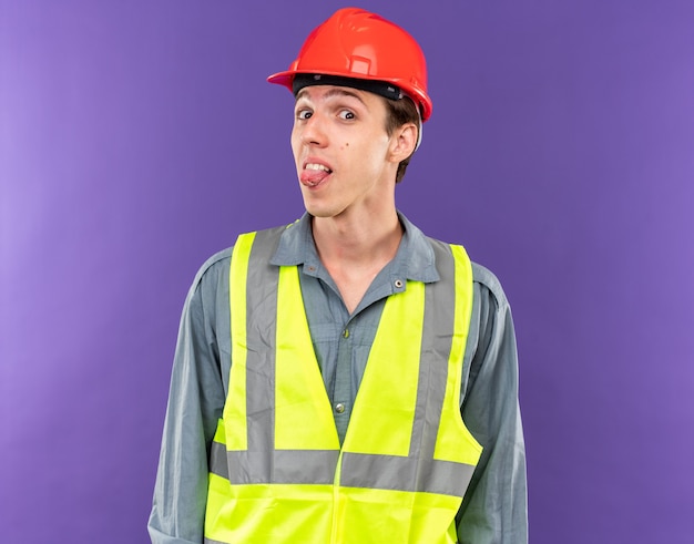 Alegre mirando a cámara joven constructor hombre en uniforme mostrando lengua