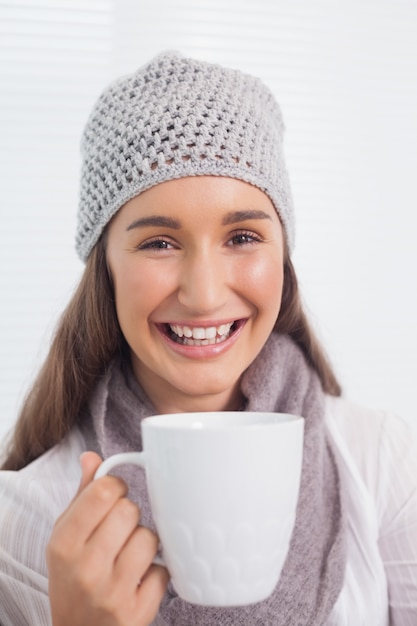 Alegre morena bonita con sombrero de invierno en la celebración de una taza de café