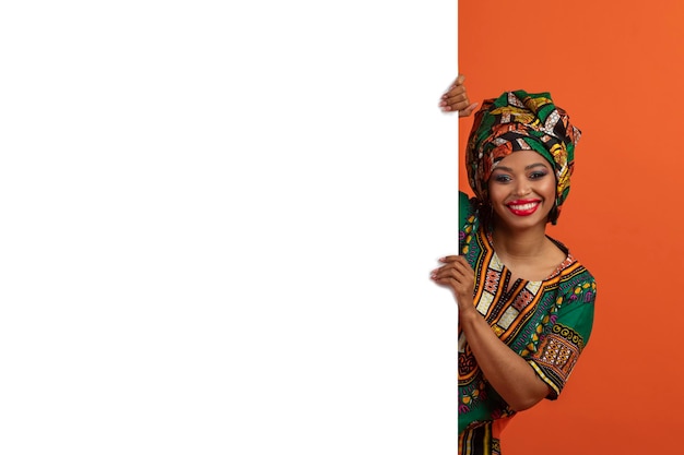 Alegre mujer africana en traje tradicional posando con tablero publicitario