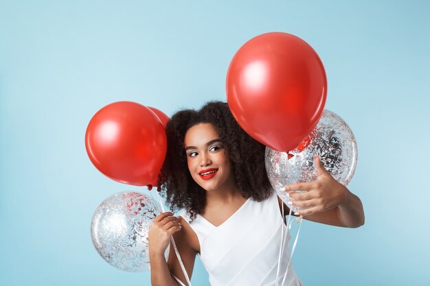 Alegre mujer africana con vestido celebrando con globos aislados