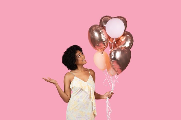 Alegre mujer afroamericana con cabello rizado mirando hacia arriba a oro rosa y globos blancos en su