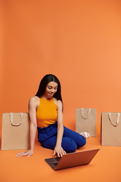 Alegre mujer afroamericana comprando en línea entre elegantes bolsas marrones