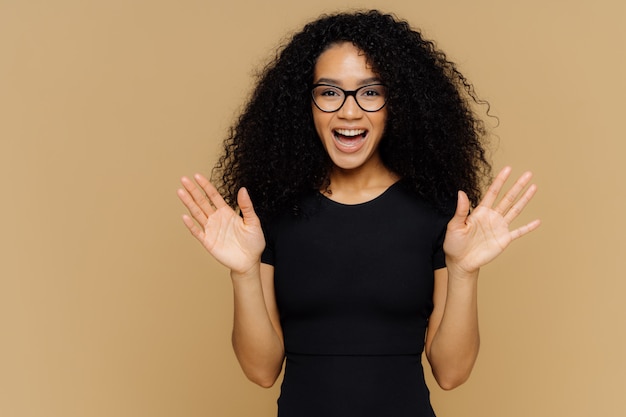 Alegre mujer afroamericana juguetona levanta las palmas, se siente emocionada, expresa felicidad