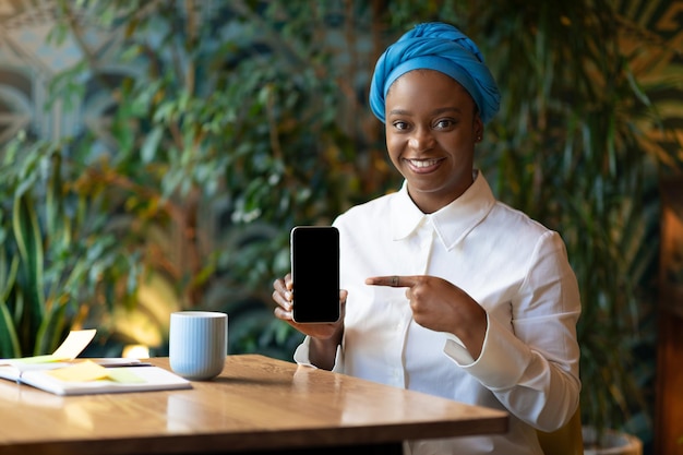 Alegre mujer afroamericana mostrando teléfono celular con pantalla vacía