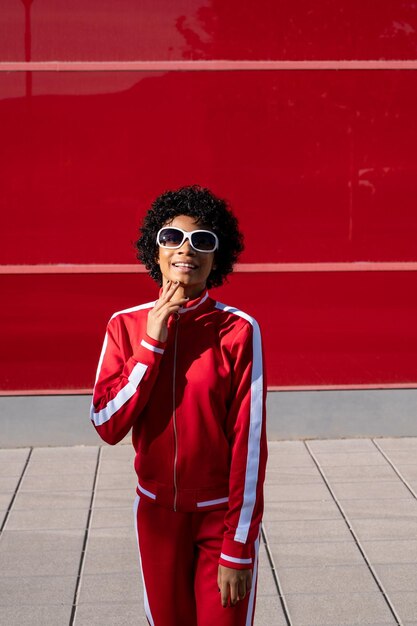 Alegre mujer afroamericana en ropa deportiva sobre un fondo rojo en un día soleado