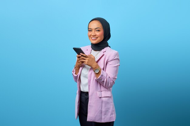 Alegre mujer asiática tiene teléfono móvil y mirando hacia arriba sobre fondo azul.