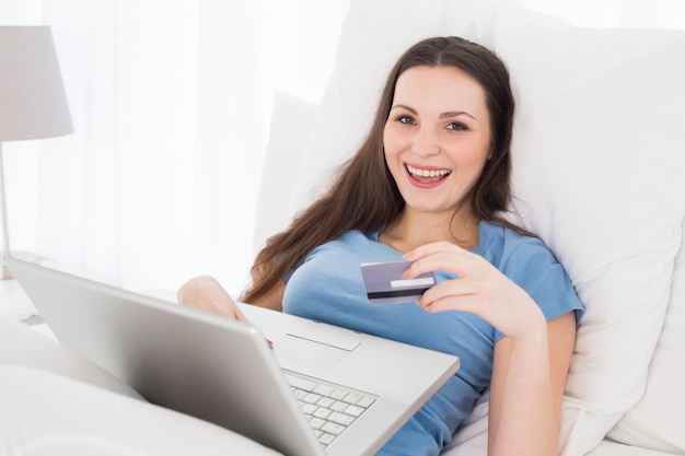 Alegre mujer casual haciendo compras en línea en la cama