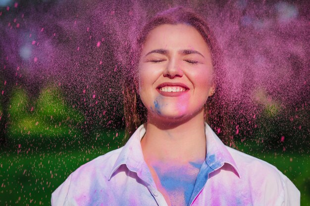 Alegre mujer caucásica posando con los ojos cerrados con explosión alrededor de pintura rosa Holi