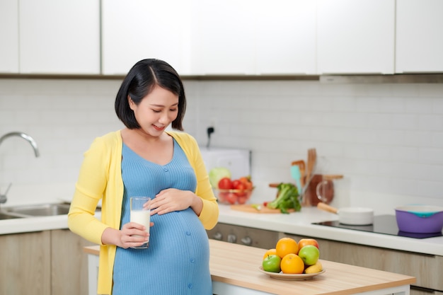 Alegre mujer esperando en su cocina bebiendo leche