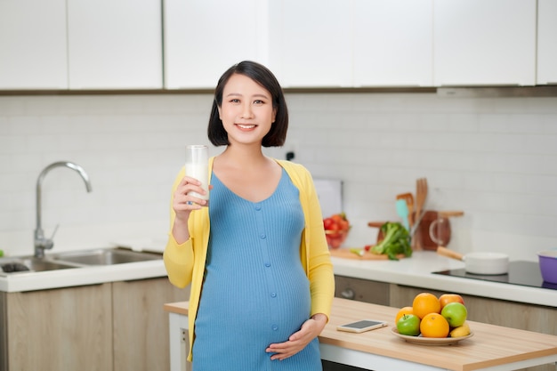 Alegre mujer esperando en su cocina bebiendo leche