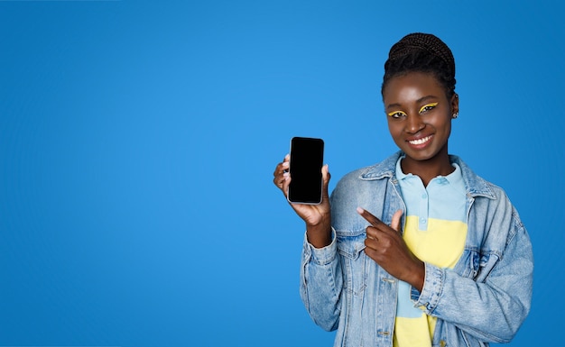 Alegre mujer joven y bonita negra apuntando a la maqueta de teléfono celular