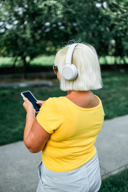 Alegre mujer madura caucásica esposa usando un teléfono móvil inteligente eligiendo la pista de sonido en línea mientras l