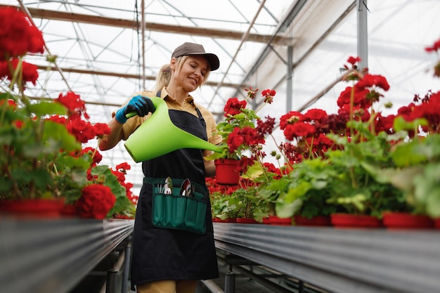 Alegre mujer madura jardinero vertiendo flores con regadera verde en invernadero