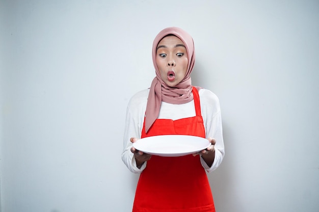 Alegre mujer musulmana asiática en delantal rojo con plato vacío Anuncio de comida Concepto de cocina