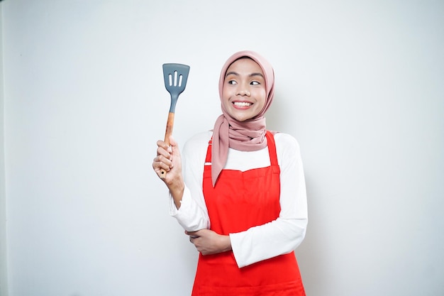 Alegre mujer musulmana asiática en delantal rojo sosteniendo una espátula Utensilios de cocina Concepto de cocina