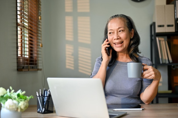 Alegre mujer de negocios asiática hablando por teléfono con alguien mientras toma un café