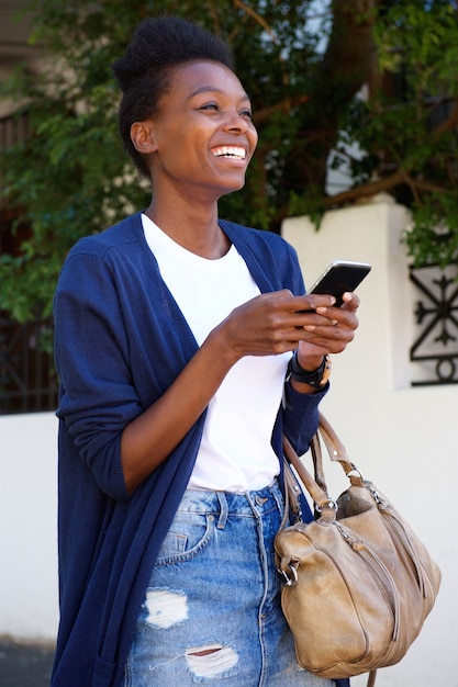 Alegre mujer negra caminando por la calle con teléfono celular