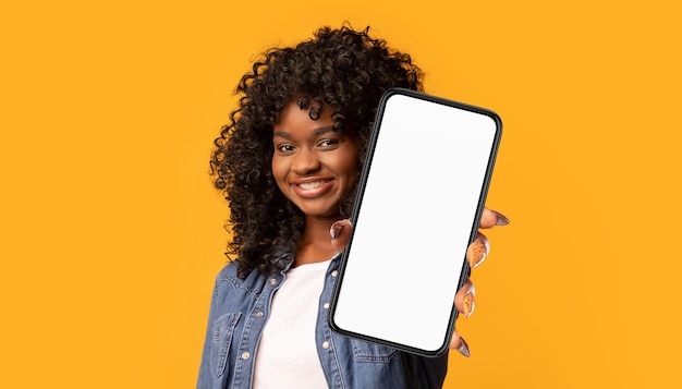 Alegre mujer negra mostrando teléfono celular en maqueta amarilla