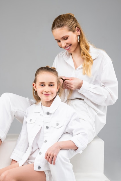 Alegre mujer de pelo largo guapa sentada detrás de su hermana pequeña y haciendo su peinado inusual