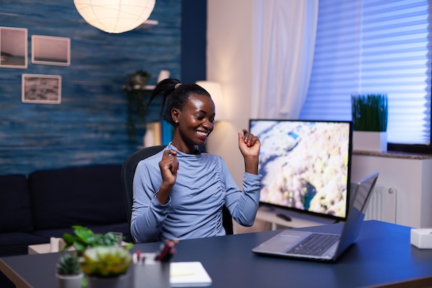 Alegre mujer de piel oscura en el curso del trabajo desde casa en la sala de estar usando la computadora portátil. La mujer negra disfruta del proceso de aprendizaje electrónico, el uso fácil de la aplicación con el tiempo.