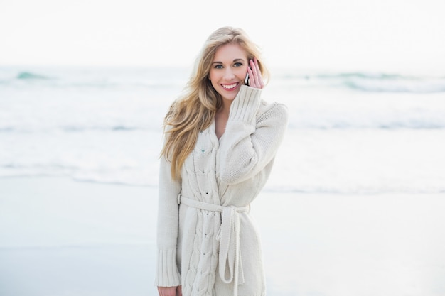 Alegre mujer rubia en cardigan de lana haciendo una llamada telefónica