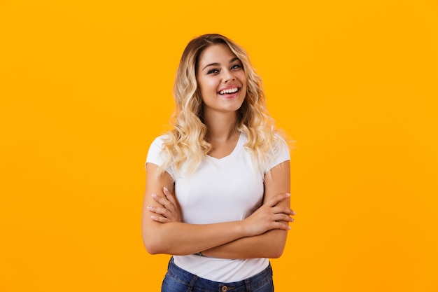 Alegre mujer rubia en ropa básica sonriendo y mirándote, aislado sobre pared amarilla