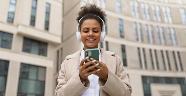 Alegre mulher afro-americana carismática ouvindo música em fones de ouvido com um telefone celular em