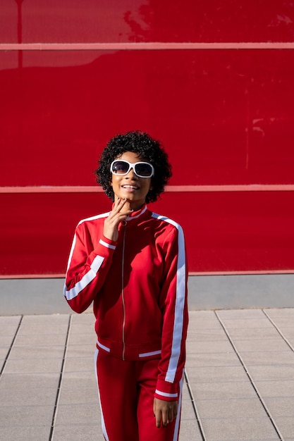 Alegre mulher afro-americana em roupas esportivas em um fundo vermelho em um dia ensolarado