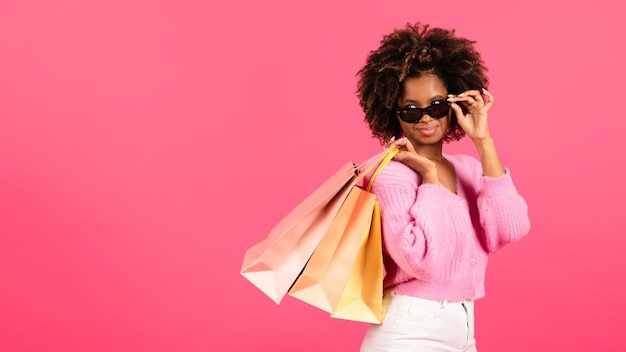 Alegre mulher afro-americana encaracolada viciada em compras tira os óculos segura muitos pacotes