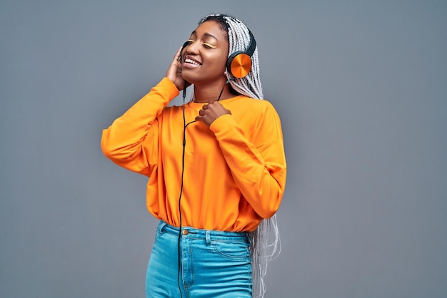Foto alegre mulher afro com olhos fechados ouvindo música em fones de ouvido sobre fundo cinza copie o espaço