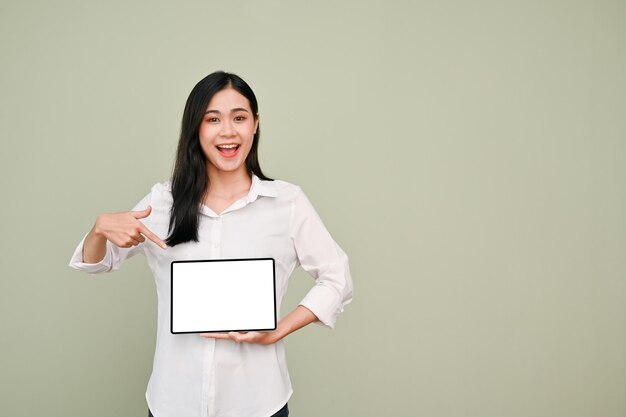 Alegre mulher asiática apontando o dedo para uma tela de tablet sobre fundo cinza