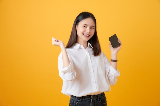 Alegre mulher asiática bonita segurando o smartphone sobre fundo amarelo claro