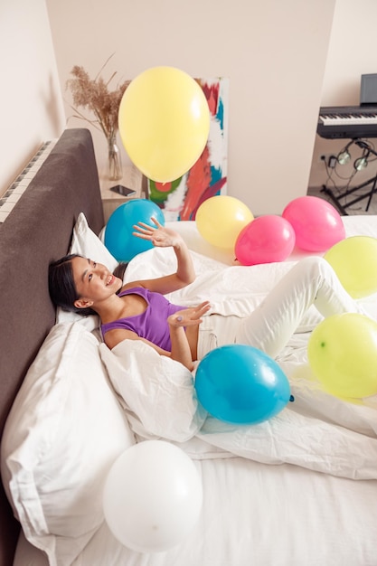 Alegre mulher asiática brincando com balões de aniversário em casa