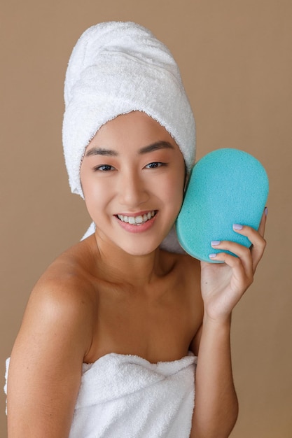 Alegre mulher asiática com esponja de banho em pé no estúdio