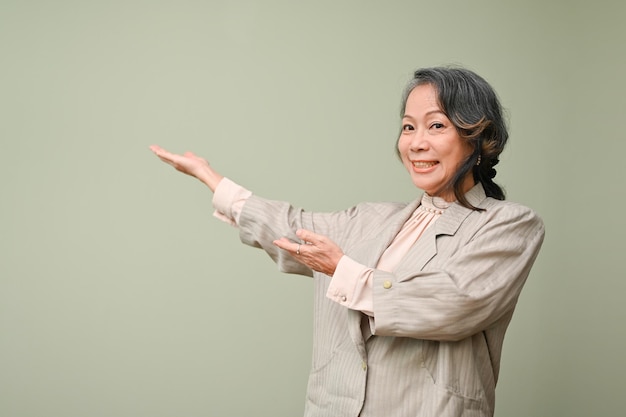 Alegre mulher asiática de 60 anos abrindo as mãos vazias de lado em fundo verde isolado