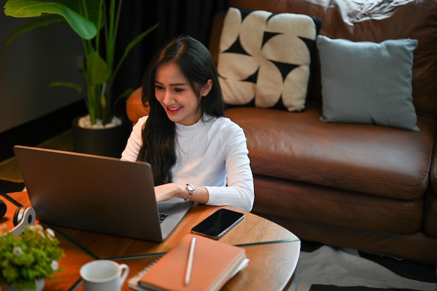 Alegre mulher asiática usando um laptop na sala de estar