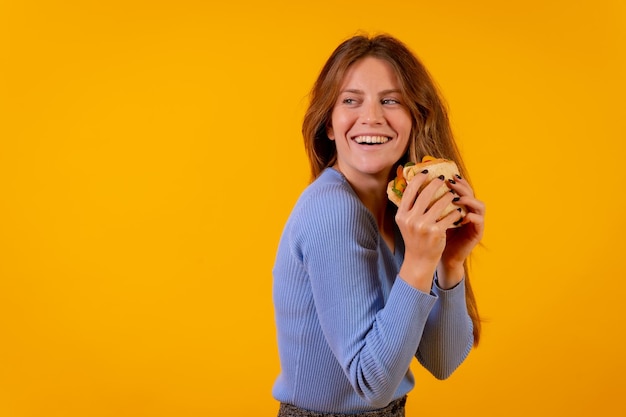 Alegre mulher comendo um sanduíche em um fundo amarelo comida saudável e vegetariana