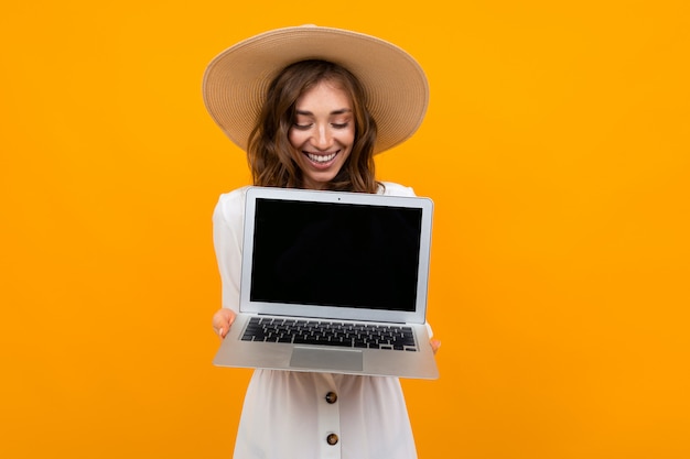 Alegre mulher de cabelos castanhos de meia idade detém um laptop em um fundo laranja