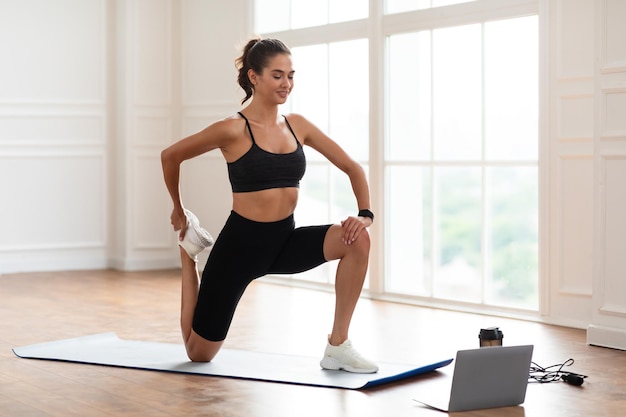 Alegre mulher esticando os músculos das pernas usando pc