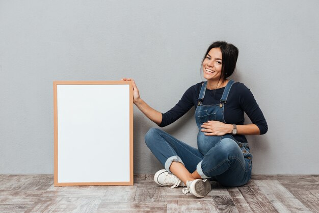 Alegre mulher grávida sentada mostrando copyspace em branco