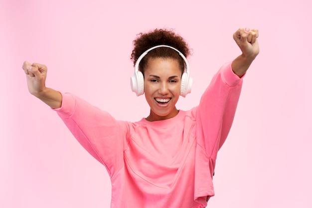 Alegre mulher multiétnica sorridente em fones de ouvido expressando felicidade sobre fundo rosa pastel