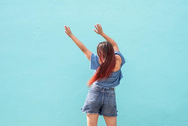 Alegre mulher na moda com cabelo vermelho dançando no fundo da parede azul na rua