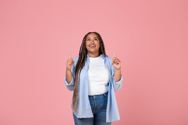 Alegre mulher obesa afro-americana apontando os dedos para cima fundo rosa