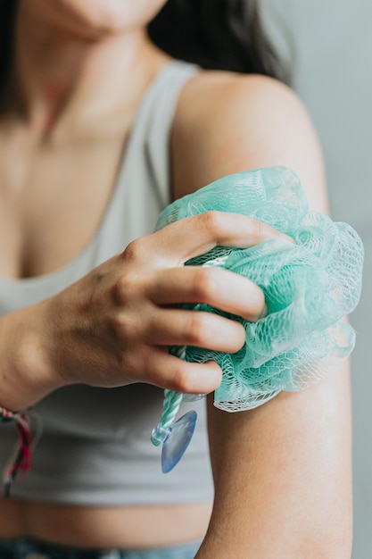 Alegre mulher segurando e usando uma esponja esfoliante descansando seu rosto Jovem adulto lavando seu corpo com bucha de banho Toalhinha esfoliante corporal closeup mãos esfregar a pele no banho Conceito de higiene pessoal