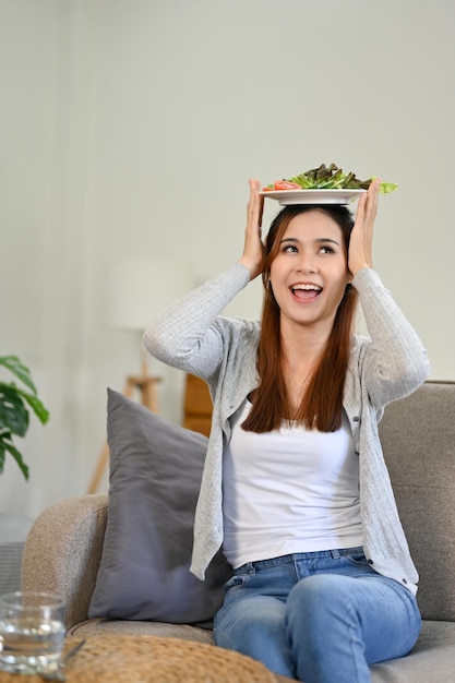 Alegre mulher sentada no sofá gosta de comer sua salada fresca e saudável Bem-estar estilo de vida