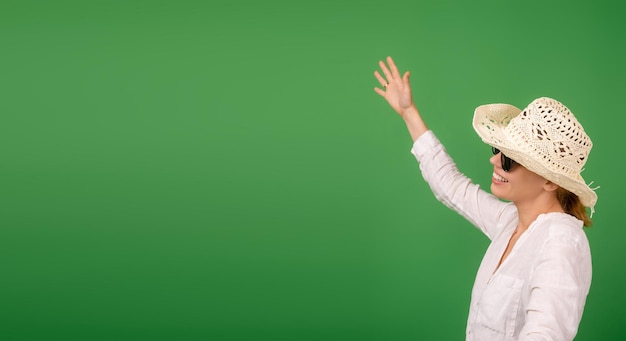 Alegre mulher sorridente em um chapéu e óculos de sol em uma camisa branca sobre um fundo verde Banner Place para o seu texto