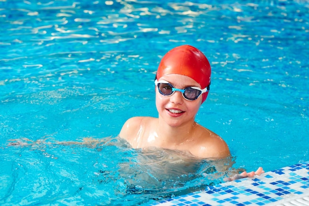 Un alegre nadador sonriente con gorra y Goggles aprende a nadar profesionalmente en la piscina del gimnasio de cerca