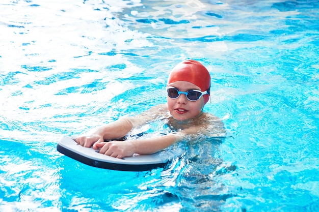 Un alegre nadador sonriente con gorra y Goggles aprende a nadar profesionalmente en la piscina del gimnasio de cerca